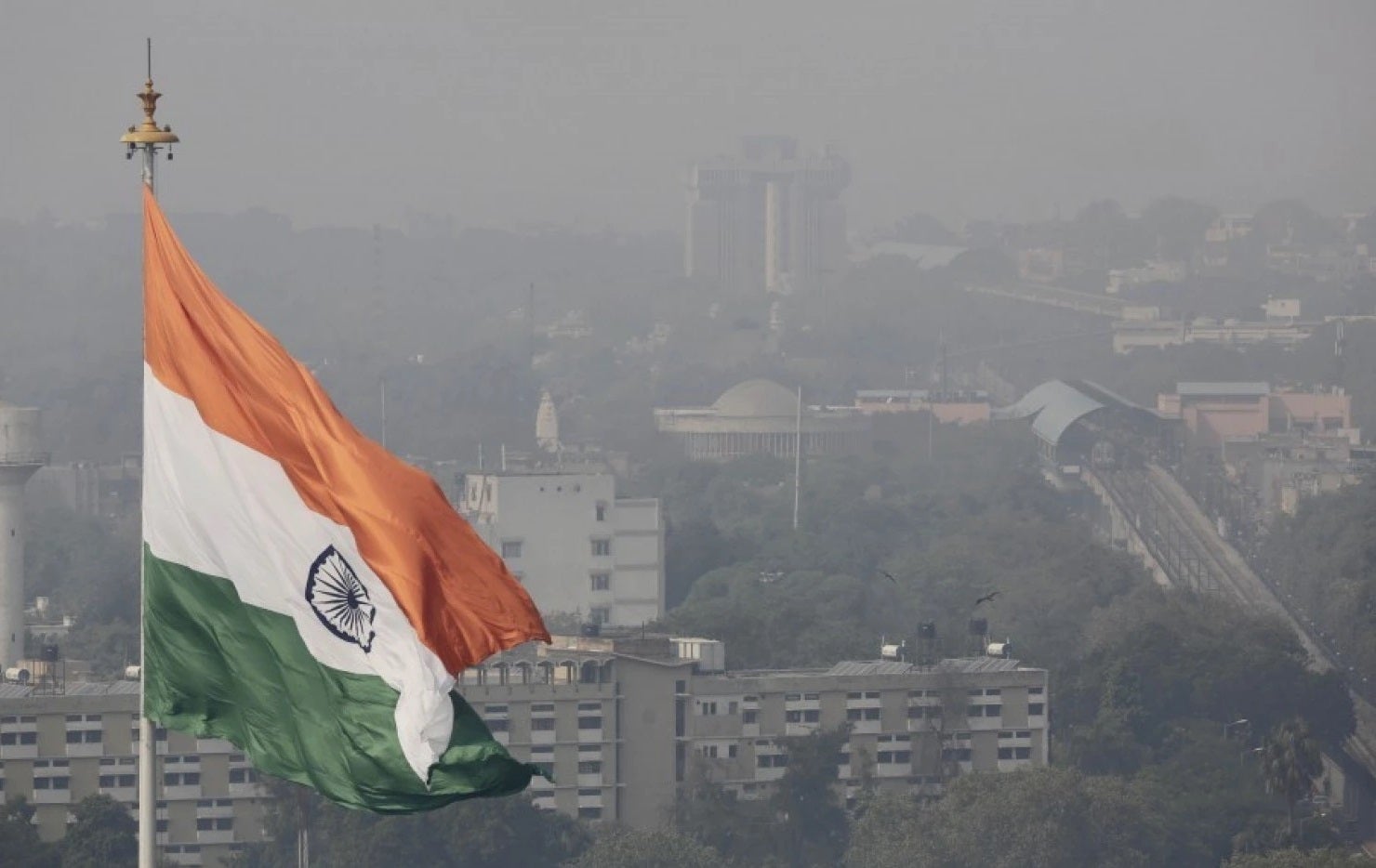 An Indian national flag flies as a thick layer of smog envelops the city skyline after Diwali festival, in New Delhi, India.