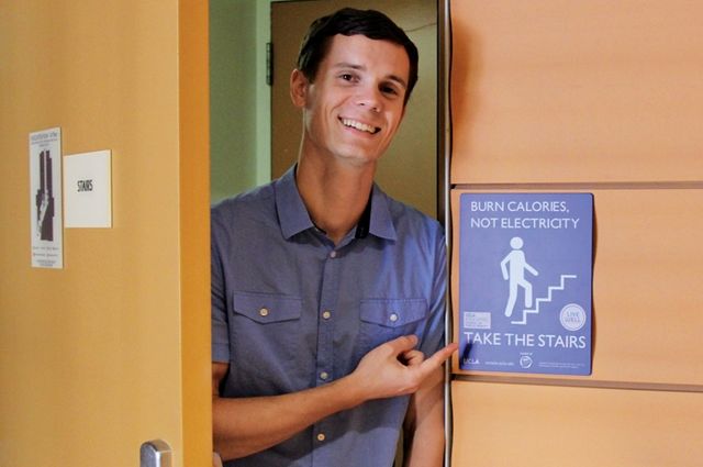 UCLA doctoral student Tyler Watson pointing at a Stair Well project sign.