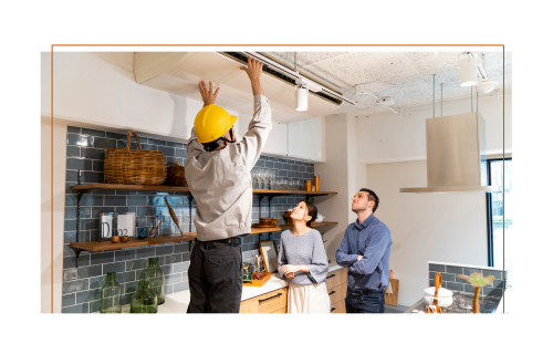 A person in a yellow hardhat installing an AC unit while a couple looks on