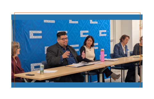 A panel of people sit a table facing an audience.