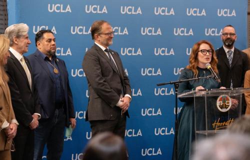 A group of people stand in front of a banner that repeats the UCLA logo
