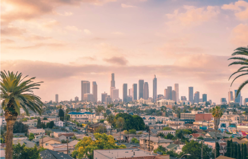 A photo of the Los Angeles skyline with pink and blue clouds and tall buildings in the background.