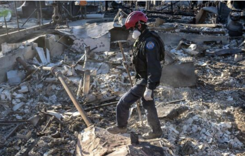 A man in a red safety helmet stands amid rubble.