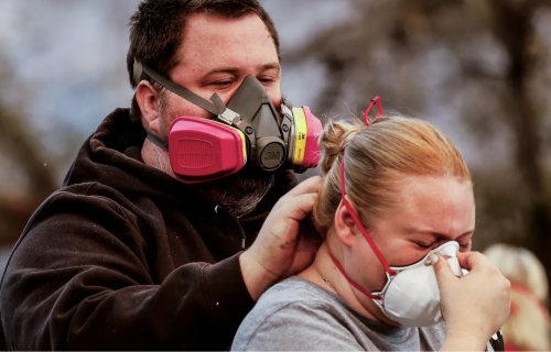 A man wearing a respiration mask helps a woman to put on a safety mask.