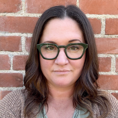 A woman with shoulder-length brown hair and glasses looking at the camera.