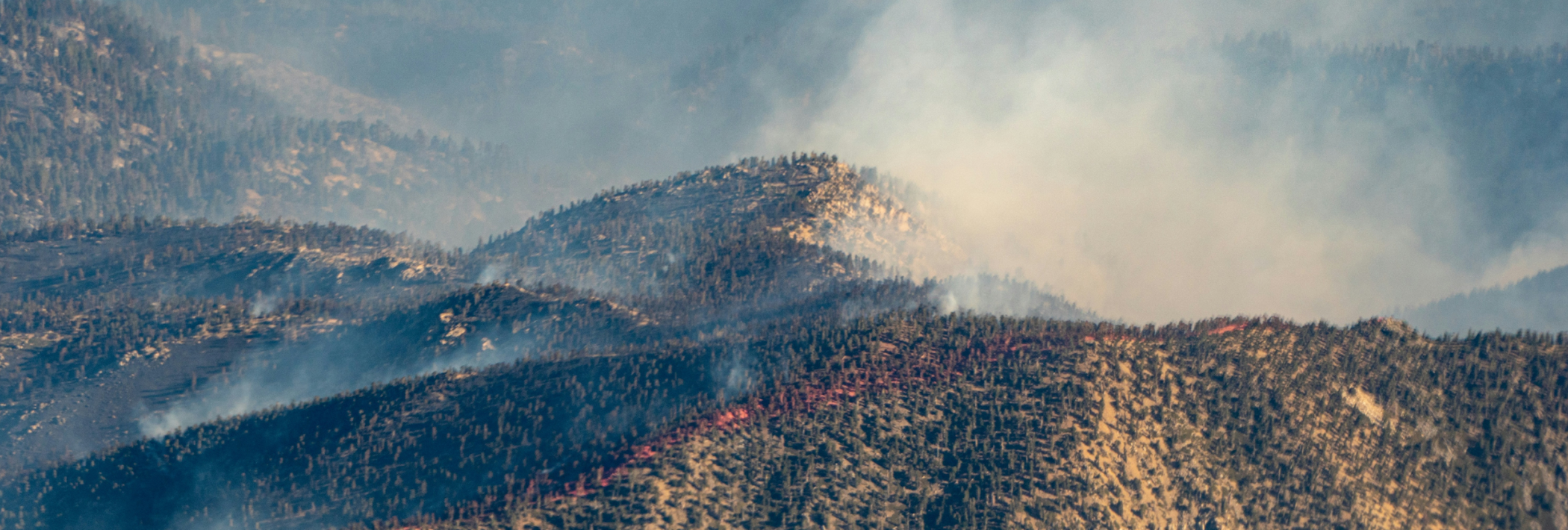 An aerial image of mountains with fire smoke billowing above them