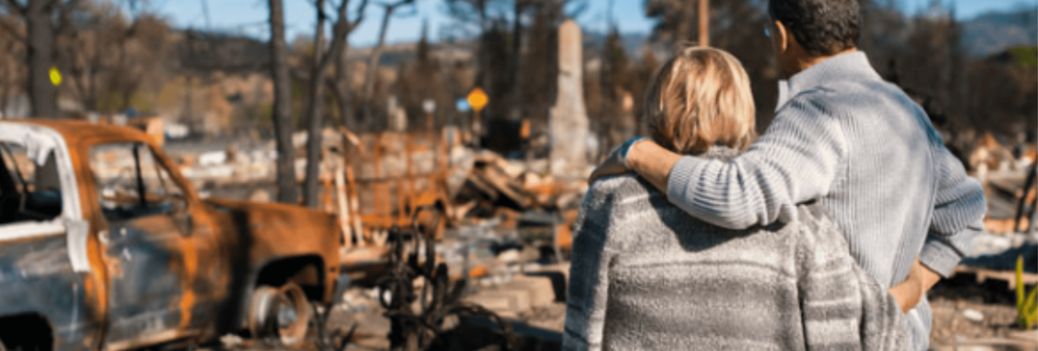 A couple stand looking at a burned down home
