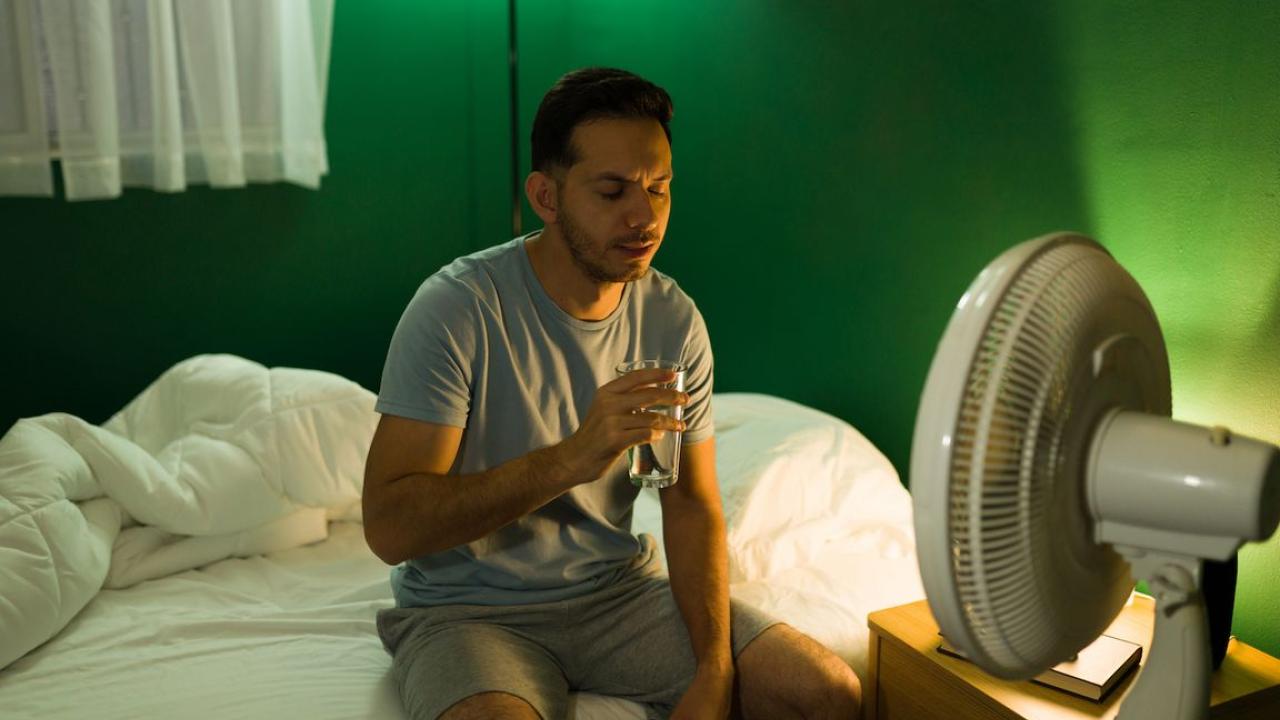 Man sitting in bed in front of a fan