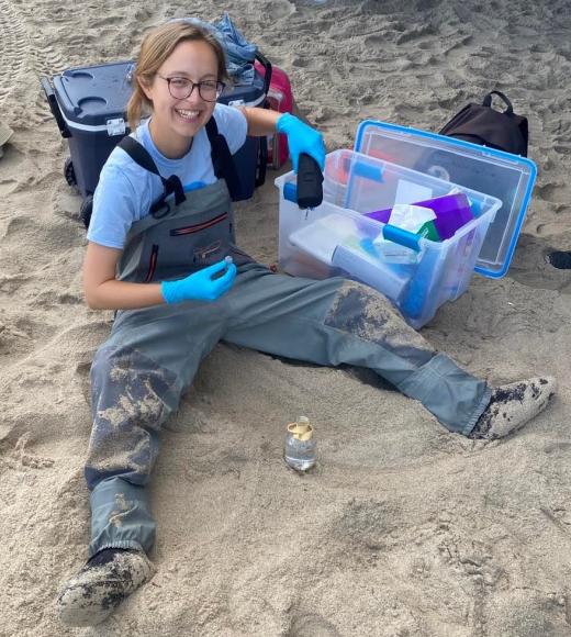 A woman sits in the sand with work overalls on collecting samples.