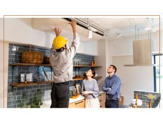 A person in a yellow hardhat installing an AC unit while a couple looks on