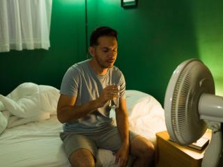 Man sitting in bed in front of a fan